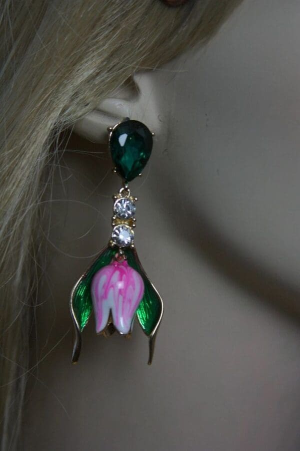 A woman wearing earrings with green leaves and pink flower.