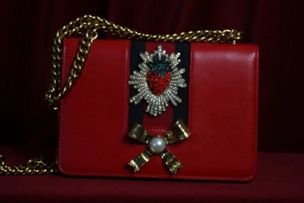 A red purse with a bow and strawberry on it.