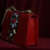 A red purse with a chain strap and a decorative flower.