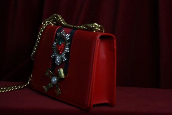 A red purse with a chain strap and a decorative flower.