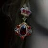 A woman wearing red and gold earrings with a crown.