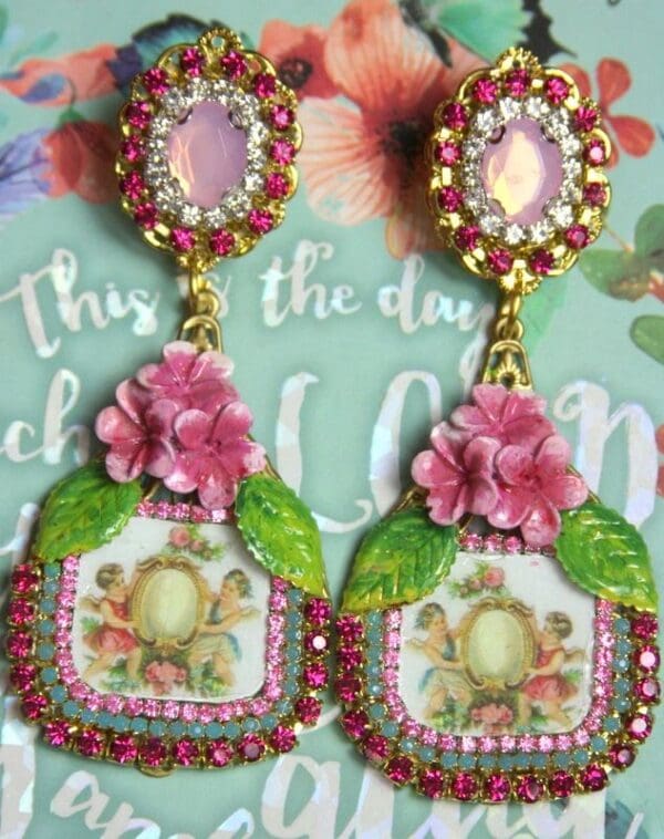 A pair of earrings with pink flowers and green leaves.