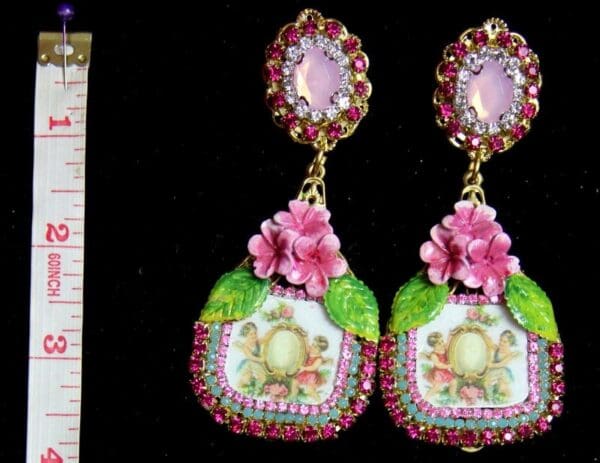 A pair of earrings with pink flowers and green leaves.