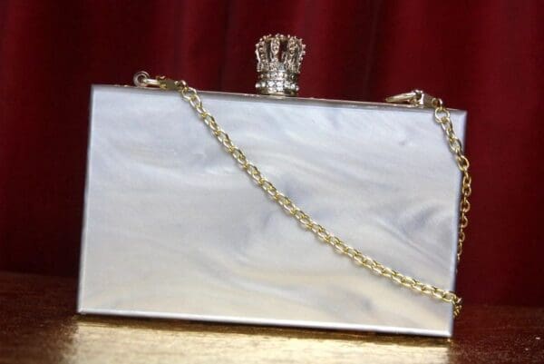 A white purse with a chain strap and a crown on top.
