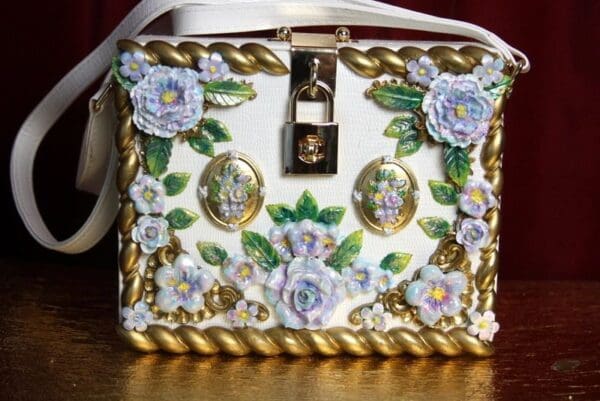 A white purse with gold trim and flowers on it.