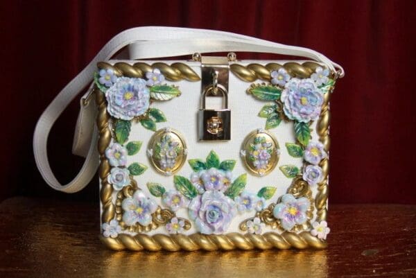 A white purse with gold trim and flowers on it.