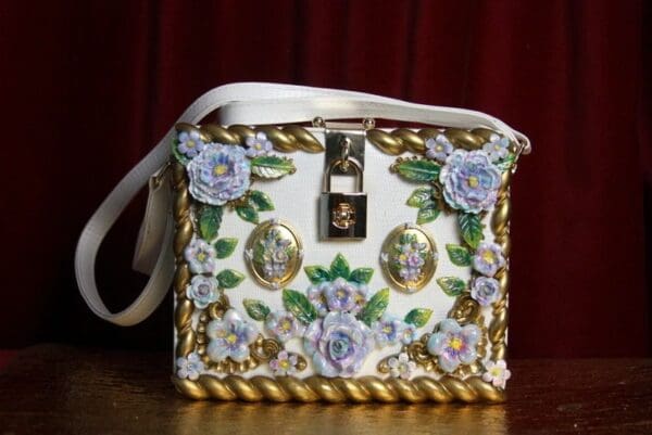 A white purse with gold and blue flowers on it.