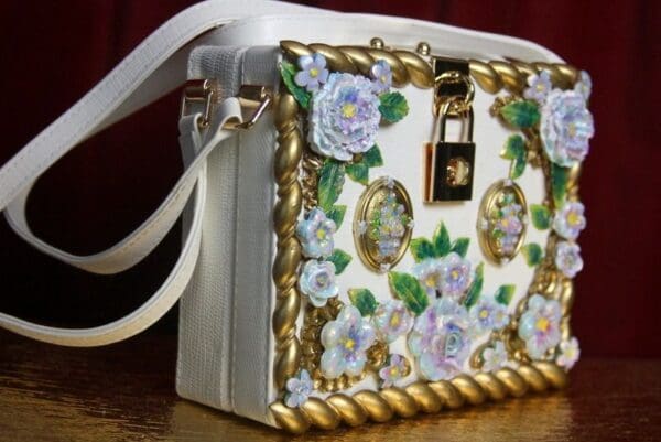 A white purse with gold trim and flowers on it.