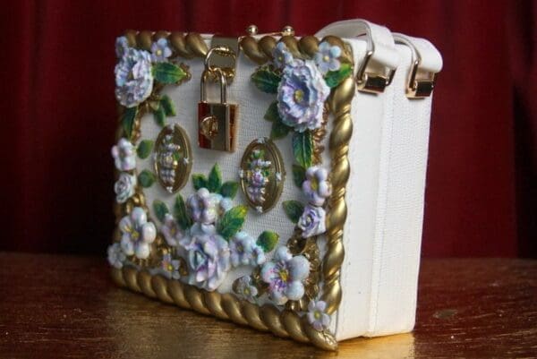 A white purse with flowers and gold trim.