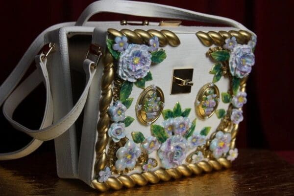 A white purse with gold trim and flowers on it.