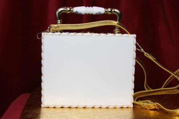 A white box bag with gold handle and chain strap.