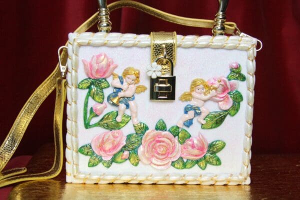 A white purse with pink flowers and angels on it.
