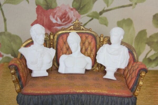 Three white busts sitting on a brown couch.