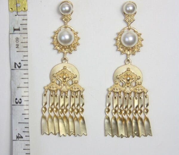 A pair of gold earrings with white pearls hanging from them.