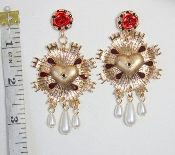 A pair of earrings with a red stone and gold tone heart.