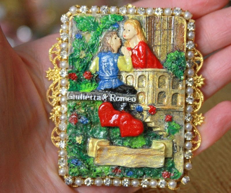 A hand holding a small painting of two people.