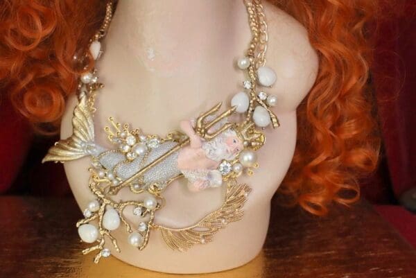 A woman wearing a necklace with white beads and gold chains.