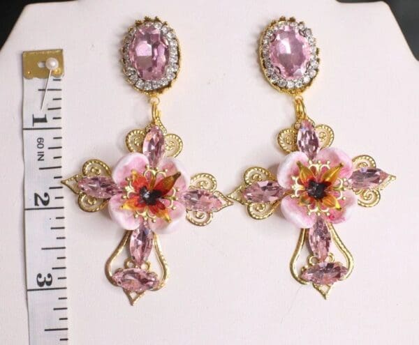 A pair of earrings with pink flowers and gold filigree.