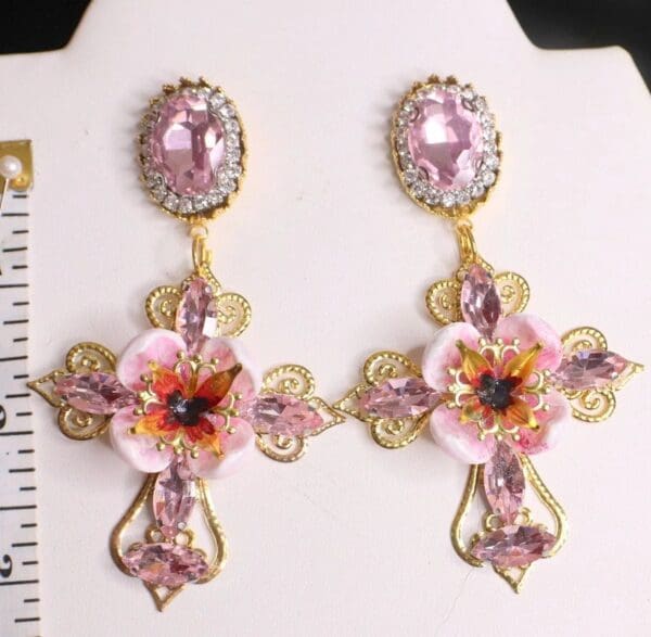 A pair of earrings with pink flowers and gold crosses.