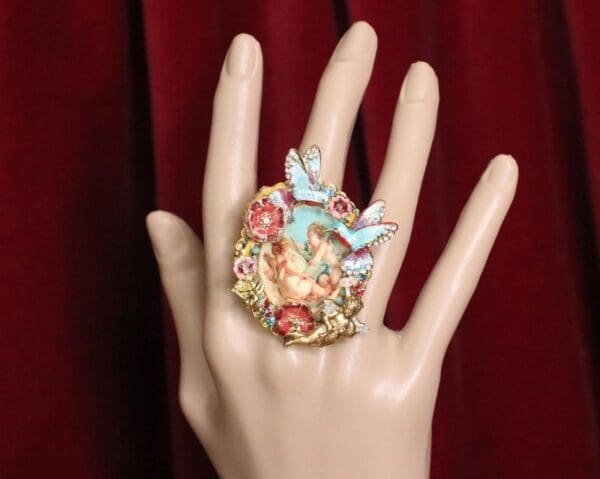A hand wearing a ring with flowers and butterflies.