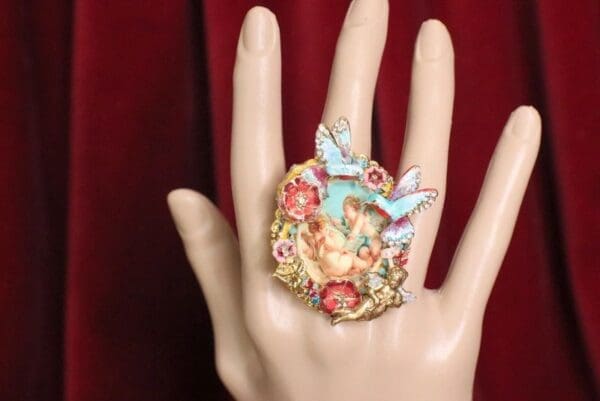 A hand wearing a ring with flowers and birds on it.