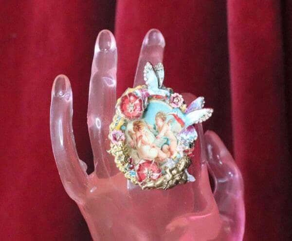 A hand holding a ring with flowers and fairies on it.