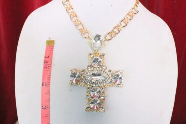 A large cross necklace with gold chain and clear stones.