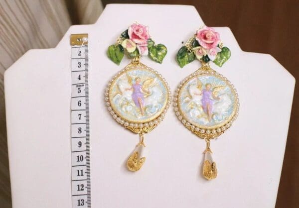 A pair of earrings with flowers and a fairy on them.