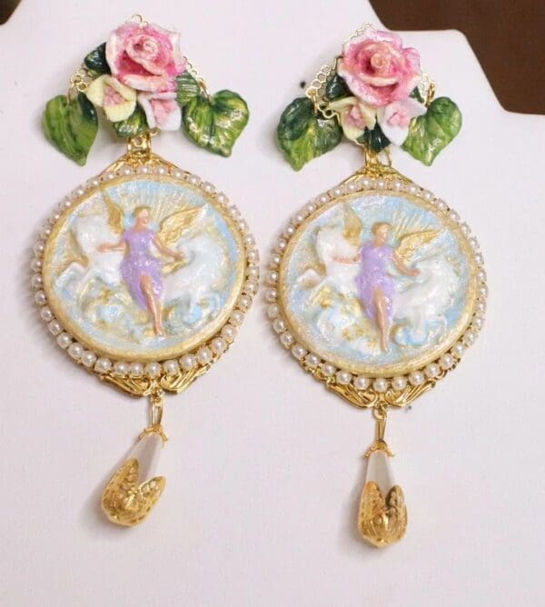 A pair of earrings with pink roses and gold angel.