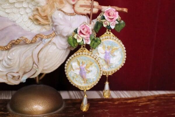 A pair of angel ornaments with roses and bells.