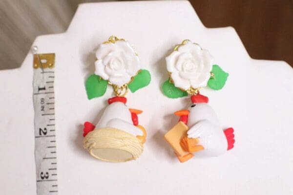 A pair of earrings with white flowers and chickens.