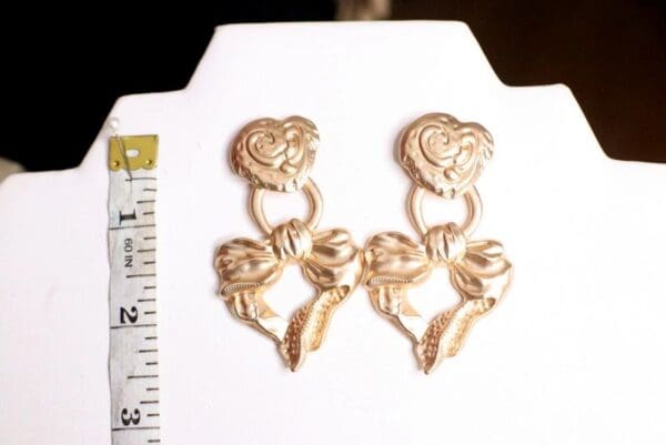 A pair of gold earrings sitting on top of a white board.