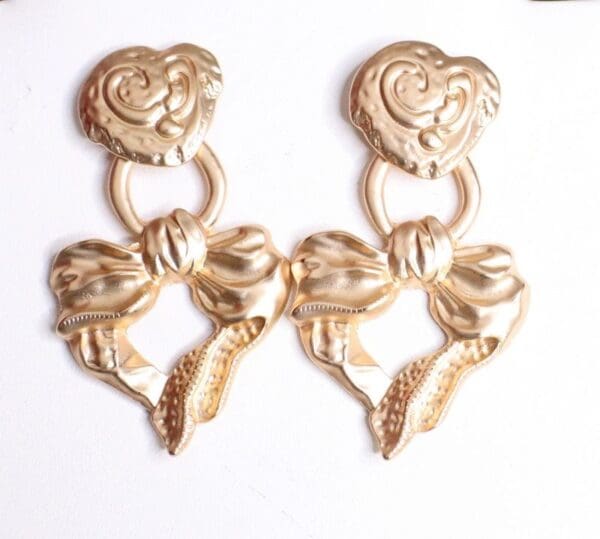A pair of gold earrings with bows and hearts.