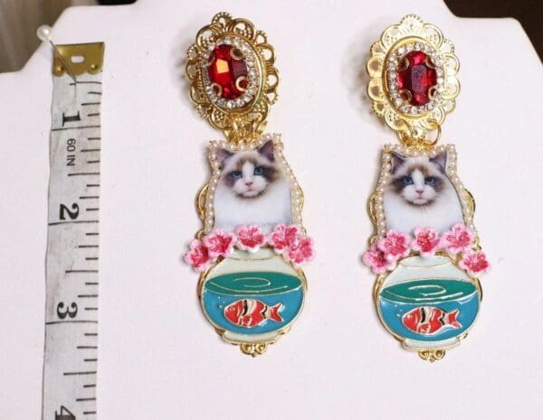 A pair of earrings with cats and goldfish on them.