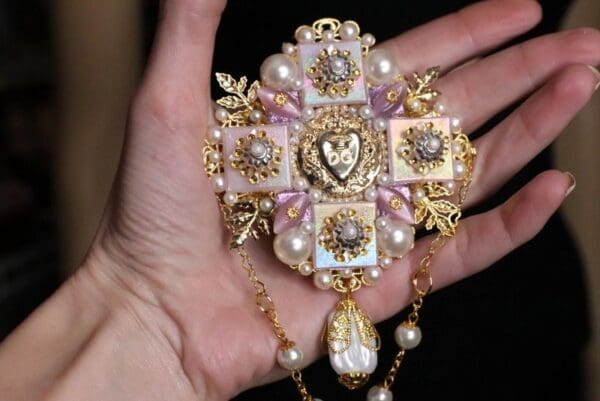 A hand holding a cross with pearls and gold