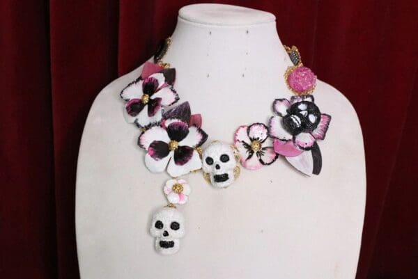 A white and pink necklace with flowers and skulls.