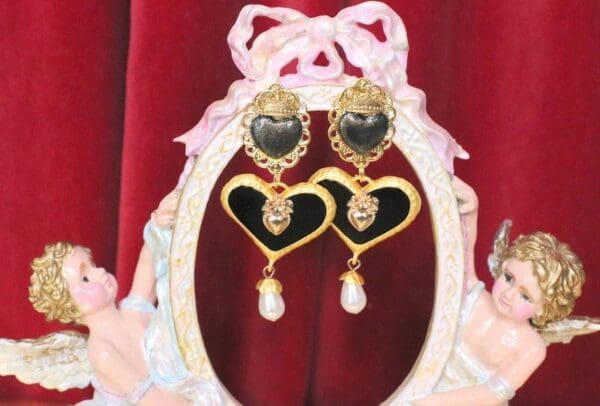 A pair of heart shaped earrings with pearls hanging from them.