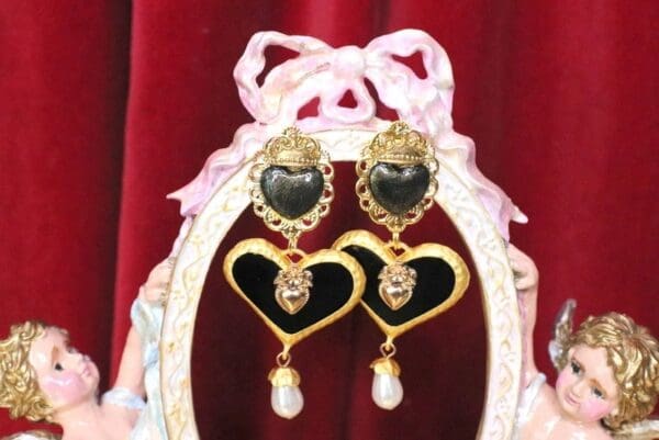 A pair of heart shaped earrings with pearls hanging from the bottom.