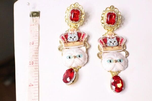 A pair of earrings with red stones and white cats.