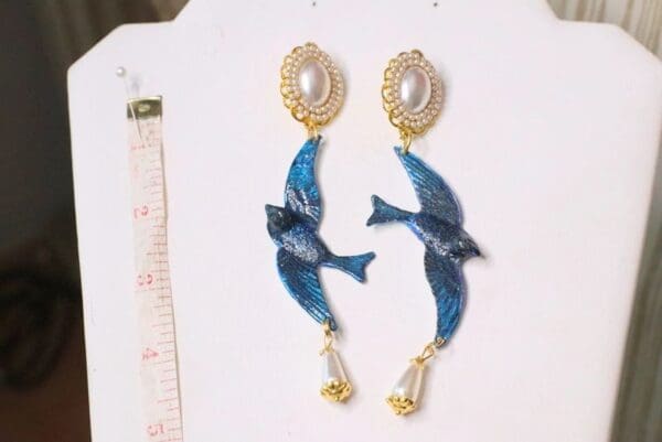 A pair of earrings with blue birds and pearls.