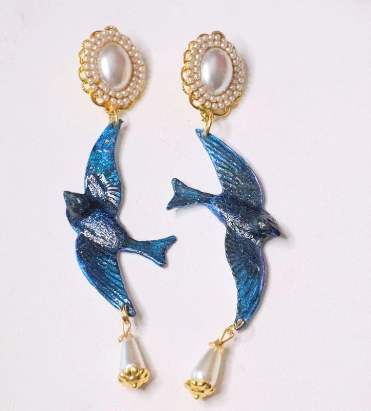 A pair of earrings with blue bird and pearls.