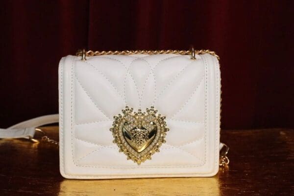 A white purse with gold chain and heart decoration.