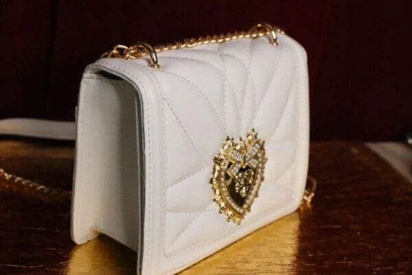A white purse with gold chain and heart on it.