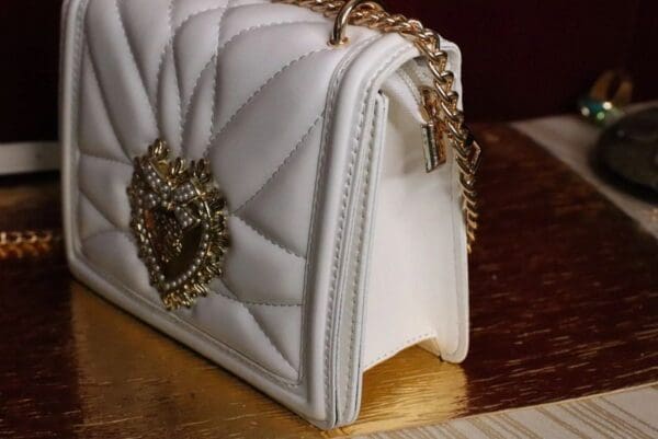 A white purse with gold chain and a heart on it.