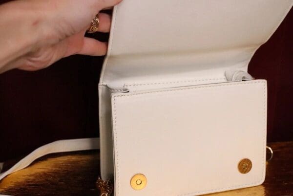 A person opening up an open white purse.