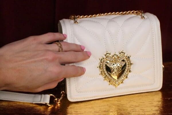 A woman 's hand is touching the heart on her purse.