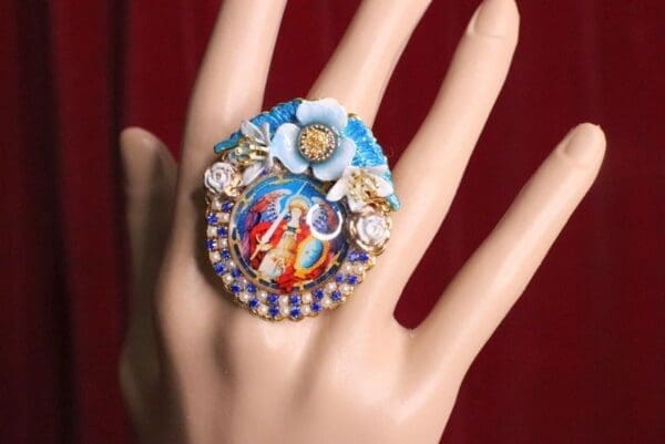 A hand wearing a ring with a picture of jesus and flowers.