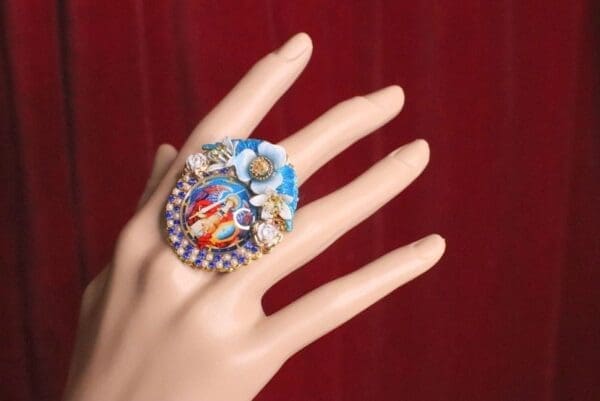 A woman 's hand wearing a ring with flowers on it.
