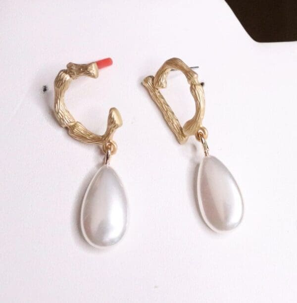 A pair of earrings with a white pearl hanging from them.