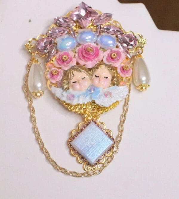A brooch with two angels and flowers on it